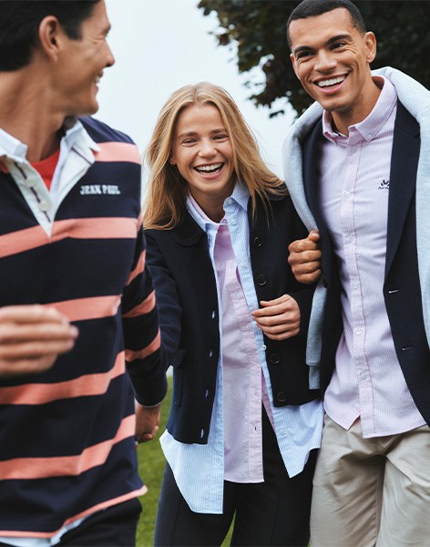 Tre personer i stilige Jean Paul-klær ved en innsjø: en mann i stripet genser, en kvinne i blazer og skjorte, og en mann i skjorte og blazer med genser over skuldrene. Perfekt for casual og klassisk stil.