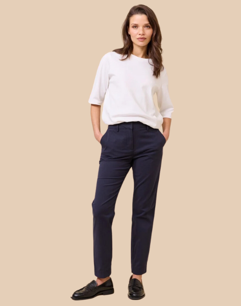 Tre kvinner iført chinos i marineblå, beige og offwhite, stylet med hvite topper og svarte loafers. Klassisk og tidløs damebukse fra Matchfashion